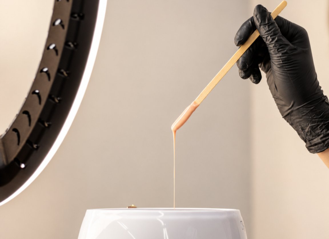 Wooden stick lifting warm wax from a wax pot, one stick per dip