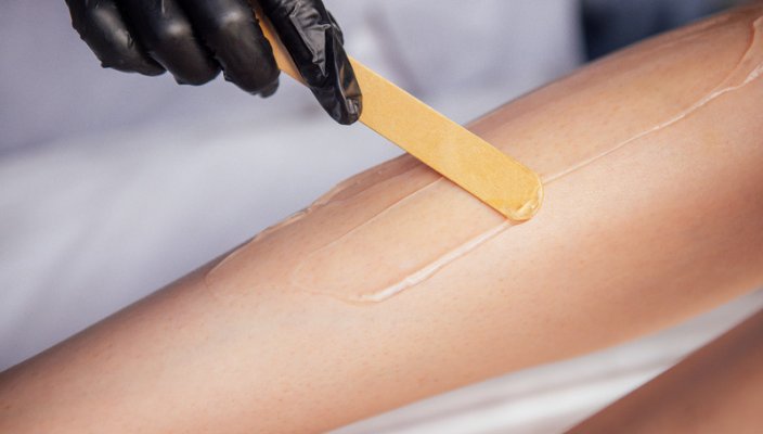Wooden applicator spreading warm wax on a guest's arm